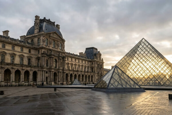 The glass pyramid entrance of the Louvre Museum at night with the historic palace wings.