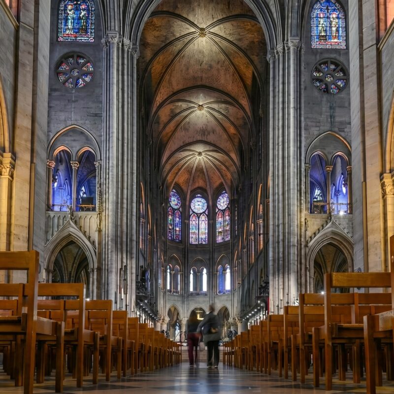 Interior of Notre Dame Cathedral showing the nave, Gothic arches and stained glass rose windows after the 2024 restoration